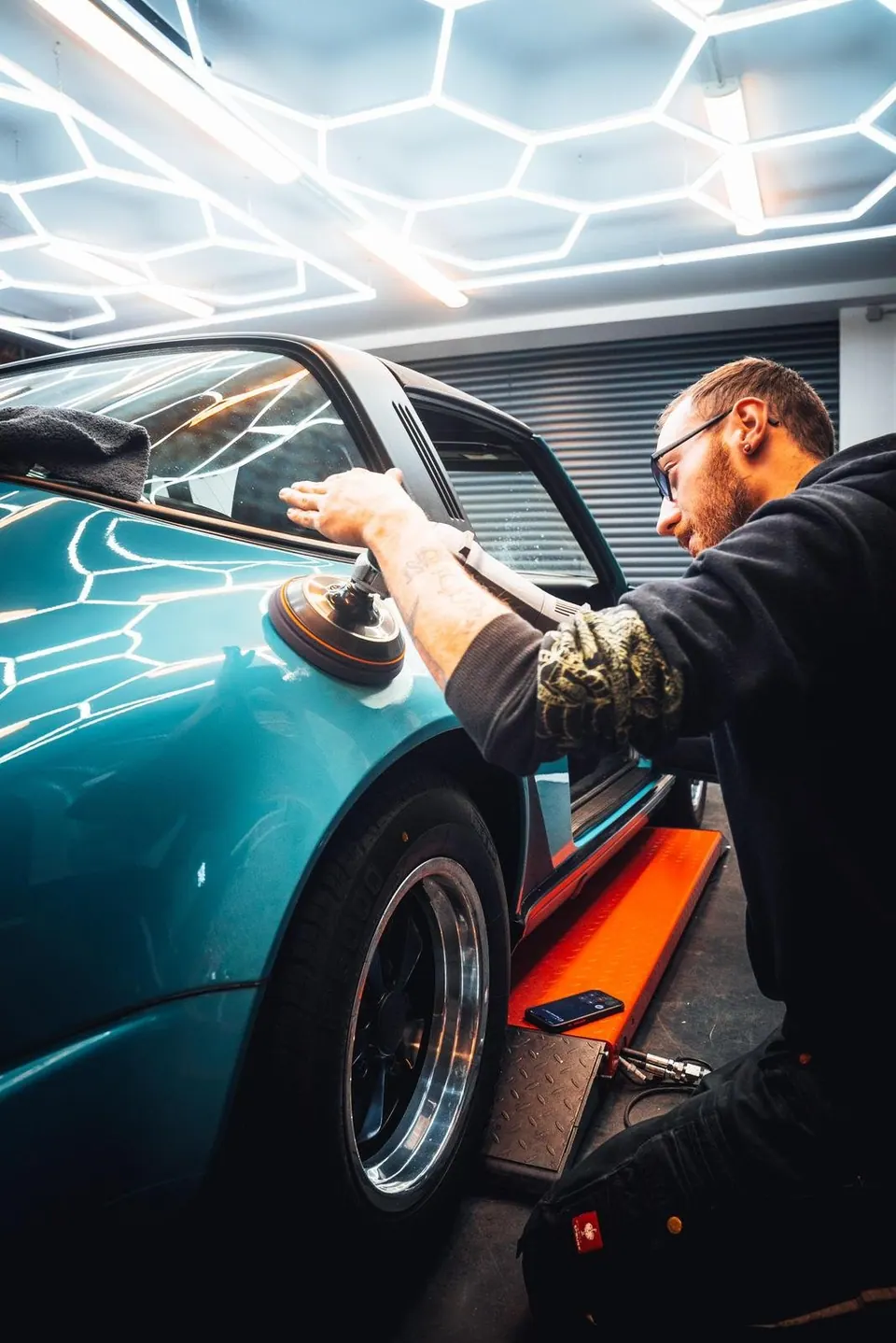 Professionelle Politur eines türkisfarbenen Autos in moderner Werkstatt mit Hexagon-Deckenleuchten